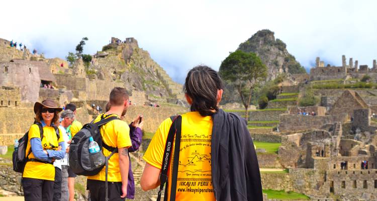 Turistas explorando ruinas antiguas con montañas al fondo.