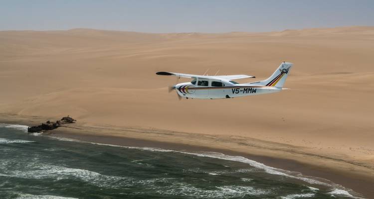 Flugzeug fliegt über Wüsten-Küstengebiet.