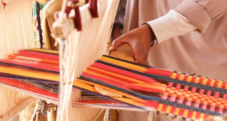 Close-up of a hand weaving colorful textiles on a loom.