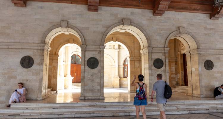 Los viajeros pasean bajo los arcos de piedra de una logia veneciana histórica.
