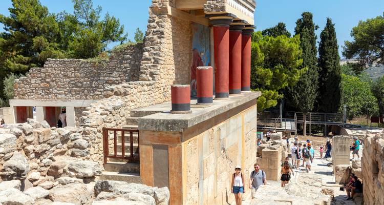 La multitud explora las estructuras de piedra y las columnas rojas del palacio de Knossos.