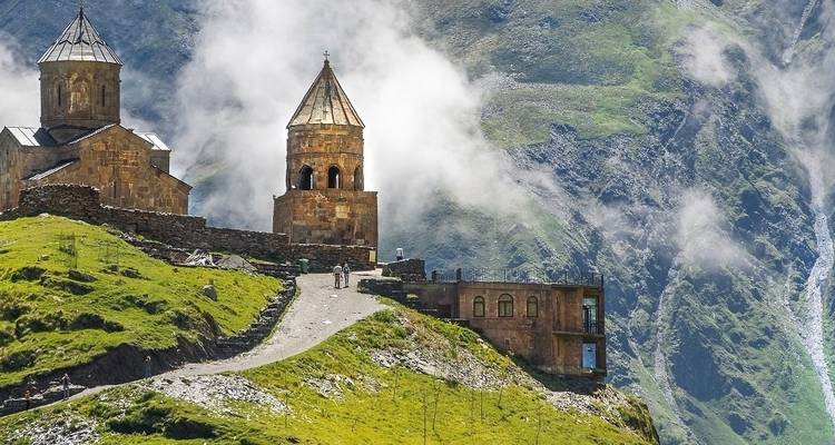 Kerken met kegelvormige daken gelegen op een heuvel met mistige bergen op de achtergrond.