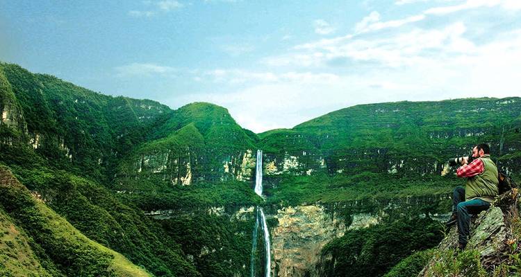 Fotograf, der einen hohen Wasserfall inmitten üppig grüner Klippen aufnimmt.