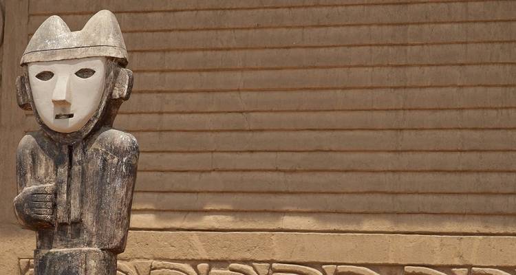 Traditionelle Statue vor einer Kulisse aus Lehmziegelarchitektur.