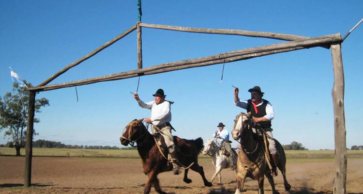 Des gauchos à cheval font des signes de la main tandis qu'ils chevauchent à travers les pampas ouvertes sous une arche en bois.