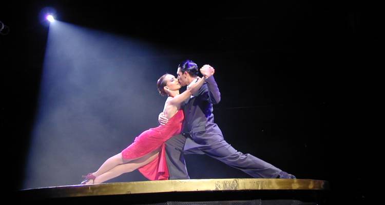 Deux danseurs de tango dans une étreinte dramatique sur une scène éclairée par un projecteur.