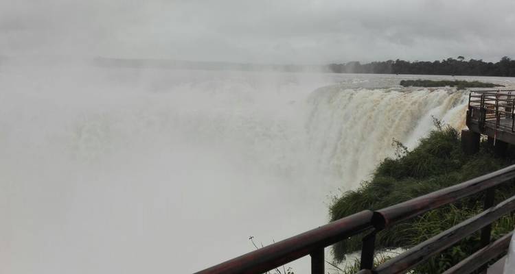Foggy view of a massive waterfall with a railing in the foreground.