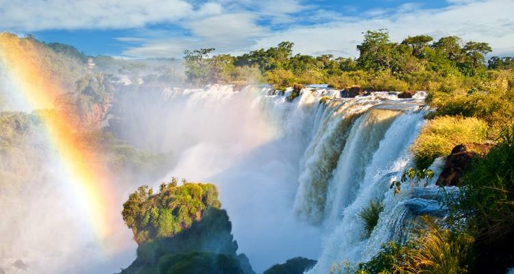 Bright waterfall with a rainbow amidst lush greenery.
