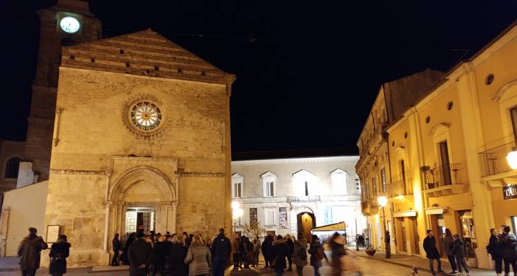 Personas reuniéndose en una plaza por la noche con edificios históricos y una torre del reloj.