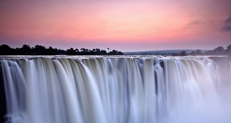 Cascade avec brume contre un ciel de coucher de soleil vibrant.