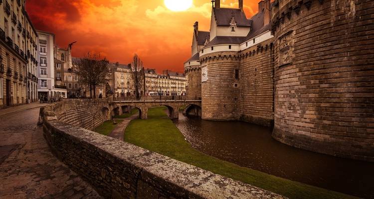 Un château avec des douves et un ciel de coucher de soleil vibrant.