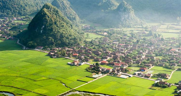 Vue panoramique d'un village niché parmi les rizières et les collines calcaires abruptes avec la brume du matin.