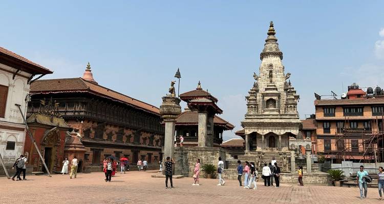 A historic square with traditional Nepalese architecture and people walking around.