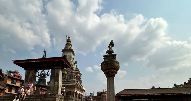 Historic Nepalese square with tourists and ancient architectural structures under a cloudy sky.