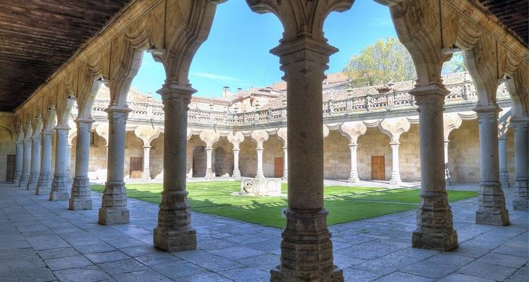 Cloister courtyard with arches and a well-kept lawn under sunlight.