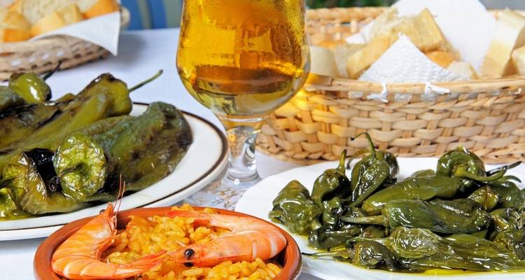 Plate of Spanish tapas with prawns and peppers, a glass of beer beside it.