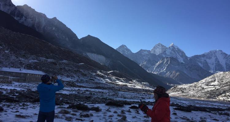 Two people capturing a scenic view of mountains with snow.