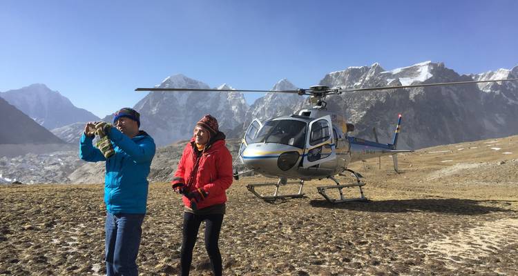 Two people near a helicopter with snowy mountains in the background.