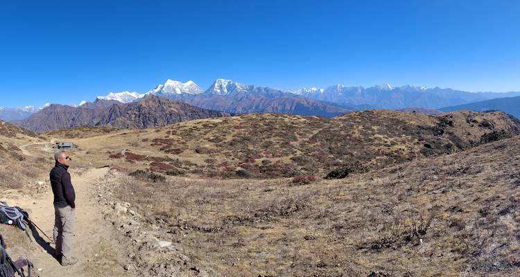 Randonneur contemplant un paysage montagneux sous un ciel bleu dégagé.