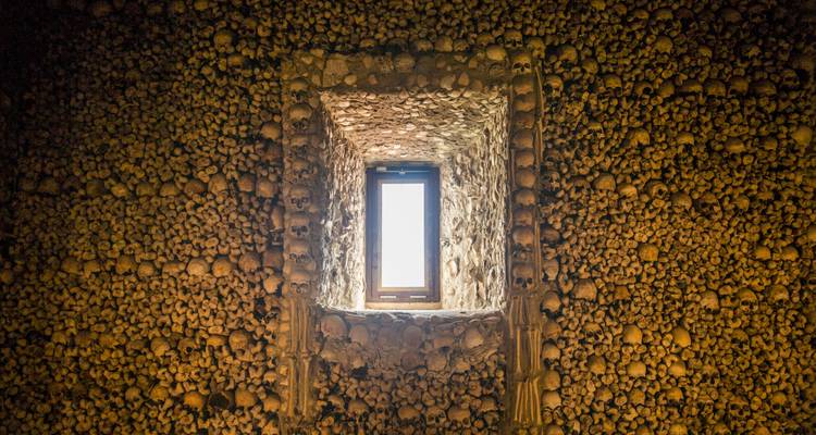 Interior de la Capilla de los Huesos de Évora con paredes completamente cubiertas de cráneos y huesos humanos alrededor de una pequeña ventana
