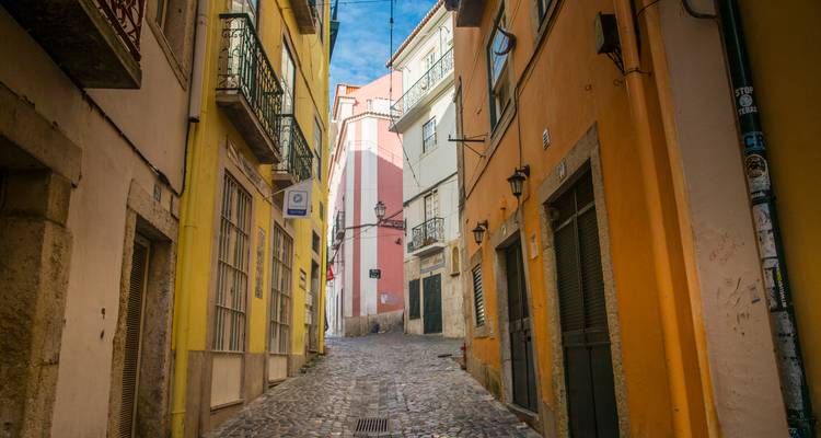 Ruelle pavée tranquille flanquée de maisons aux couleurs jaune vif et orange menant vers le ciel bleu en montant.
