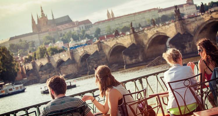 People enjoying a riverside view of a historic city with a bridge.
