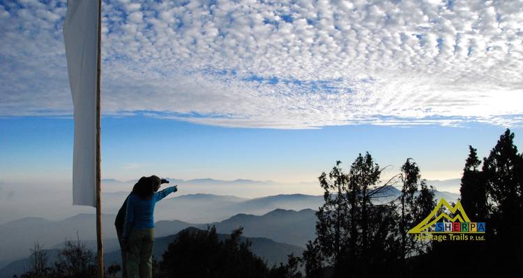Personne pointant vers un paysage de montagne sous un ciel à motifs.