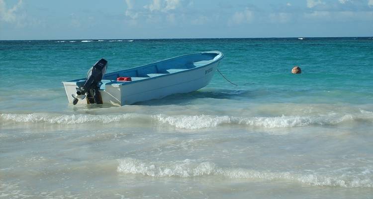A small boat anchored in a clear blue sea with sandy shores.