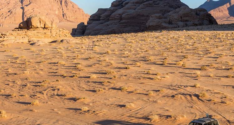 Een 4x4-voertuig rijdt door de gouden duinen en imposante rotsformaties van Wadi Rum bij zonsondergang.