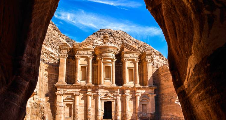 Fachada icónica del Monasterio de Petra enmarcada dramáticamente por estrechas paredes del cañón bajo un cielo azul vívido.