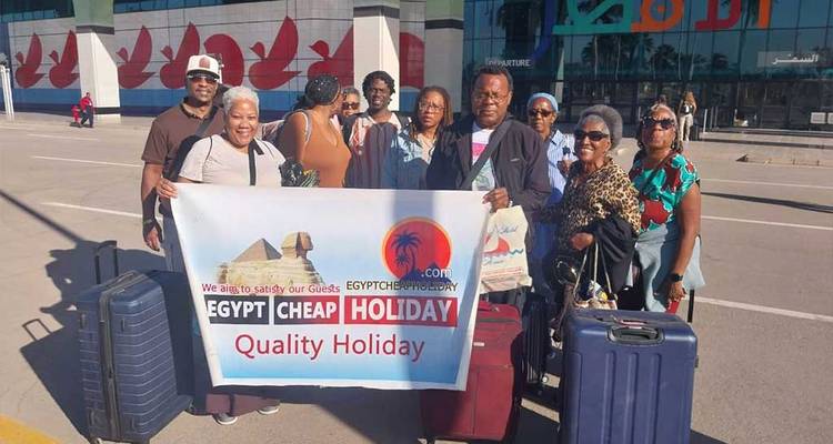 Groep toeristen met bagage poseert met een 'Goedkope Vakantie' banner op een luchthaven.