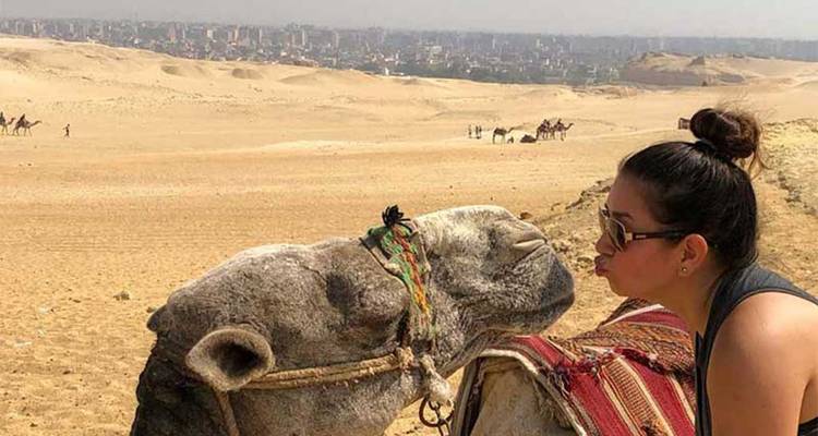 Vrouw die speels interacteert met een kameel op het woestijnzand.