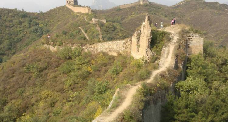 Wanderer auf einem hügeligen Abschnitt der Chinesischen Mauer mit Vegetation.