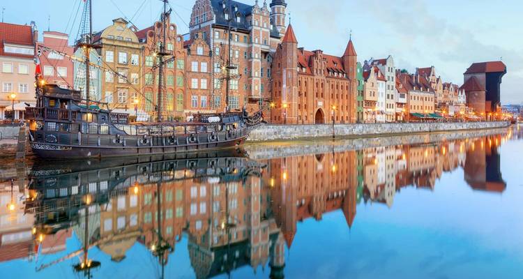 Bâtiments historiques colorés se reflétant dans l'eau avec un navire classique à Gdansk.