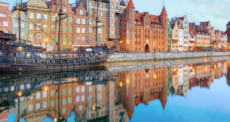 Des bâtiments historiques colorés et une réplique de galion se reflètent parfaitement dans la rivière calme de Gdansk à l'aube