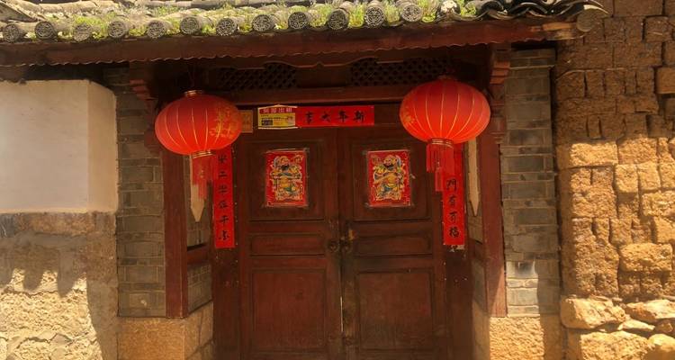 Une porte traditionnelle en bois encadrée par des murs de briques et deux lanternes rouges avec de brillants distiques de festival.