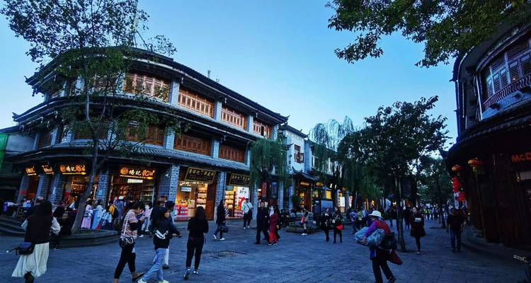 Scène de soirée dans une vieille ville chinoise historique avec des rues pavées, des devantures de magasins éclairées et de nombreux visiteurs qui se promènent.