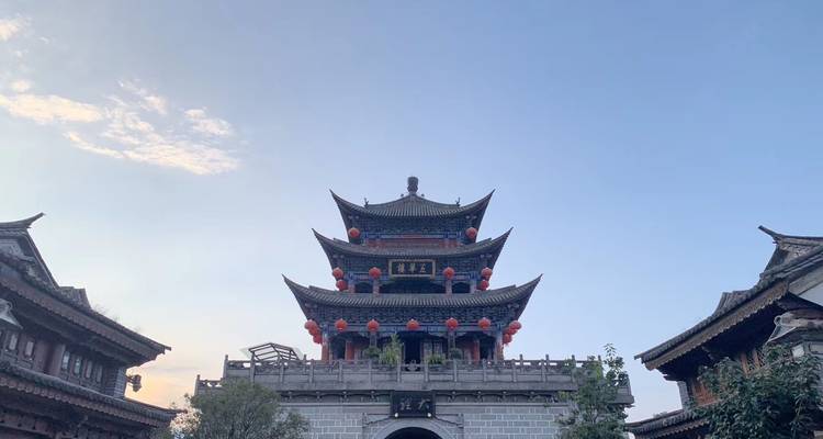 Une tour de porte ancienne à plusieurs niveaux décorée de lanternes rouges se dresse contre un ciel du soir bleu clair.