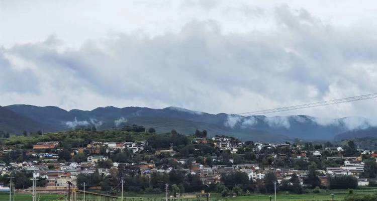Une ville étalée au pied de montagnes brumeuses sous un ciel nuageux dans la campagne du Yunnan.