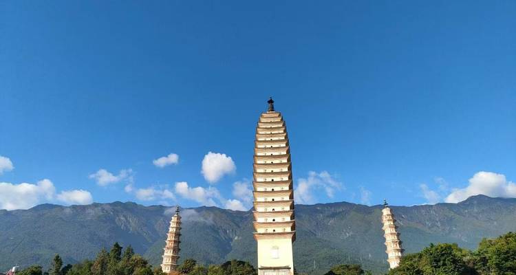 Trois pagodes élancées s'élèvent de façon spectaculaire contre un ciel bleu sans nuages avec des montagnes au loin.