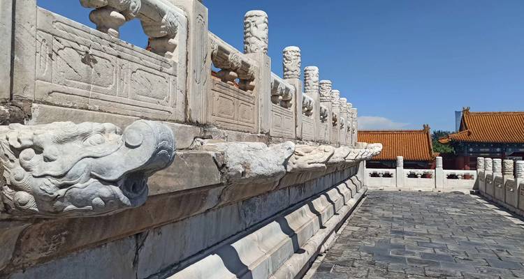 Gros plan de sculptures en pierre sur un pont avec des bâtiments traditionnels en arrière-plan.
