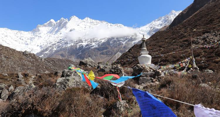 Banderas de oración coloridas y una estupa blanca recortadas contra los dramáticos picos nevados del Himalaya.
