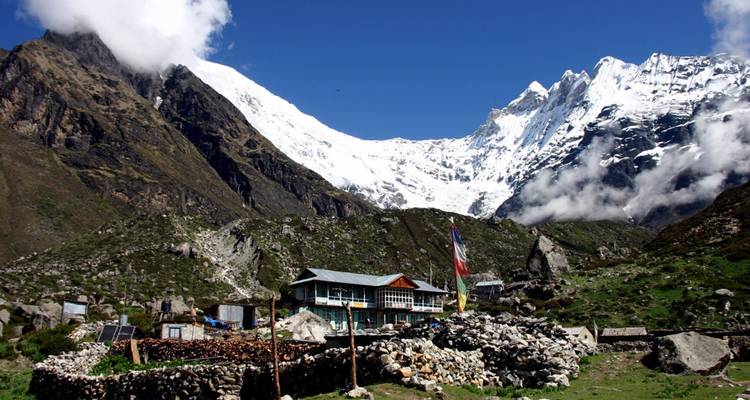 Picos del Himalaya cubiertos de nieve se alzan sobre un pequeño pueblo de piedra bajo un cielo azul brillante.