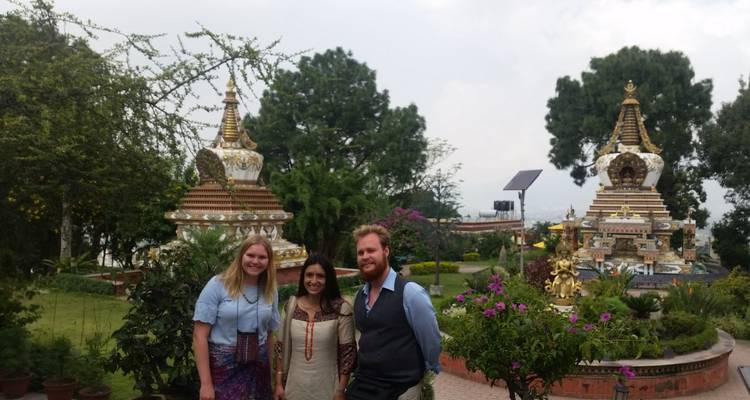 Tres viajeros sonríen para una foto en un jardín con estupas ornamentales y flores en floración.