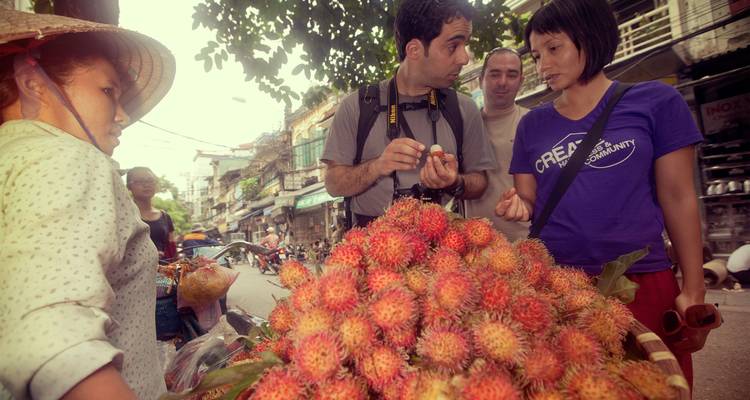 Viajeros probando fruta de rambután fresca en un mercado callejero muy concurrido.