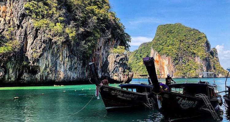 Los tradicionales barcos de cola larga flotan en aguas cristalinas frente a acantilados de piedra caliza dramáticos y jungla.