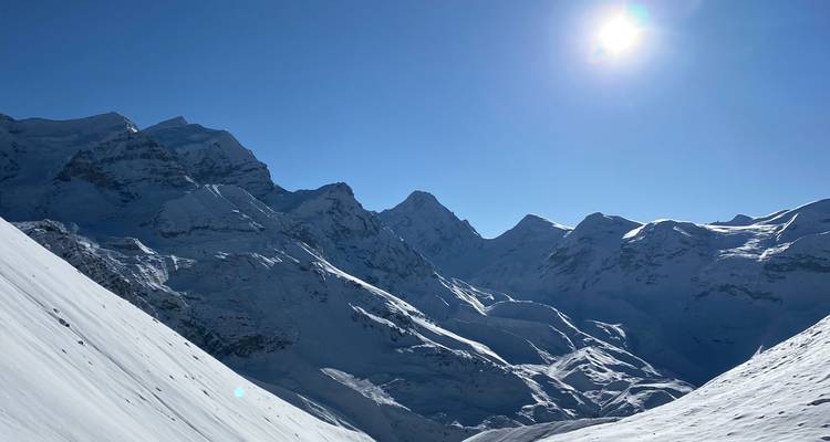 Sol brillante que resplandece sobre una cordillera prístina cubierta de nieve con cielo azul profundo y picos escarpados.