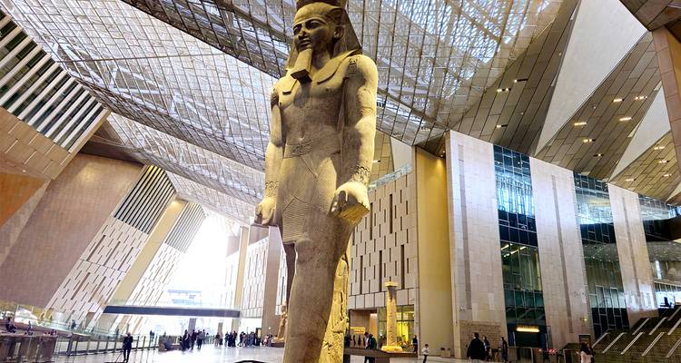 Een groot oud standbeeld binnen een modern architecturaal gebouw.