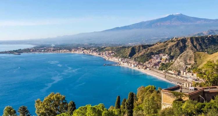 Kustpanorama van een turquoise baai en historische stad met uitzicht op de Mount Etna.