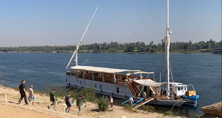 A traditional boat docked on the Nile River with people nearby.